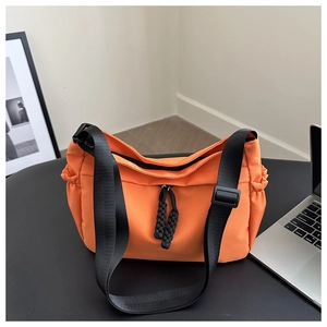 Detail view of orange nylon tote bag with black wide shoulder strap and drawstring pockets
