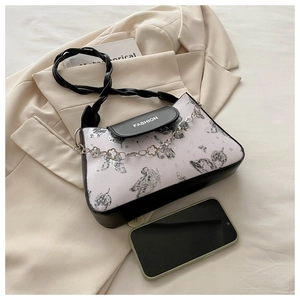Detail of crossbody bag with butterfly print, woven handle, and floral metal chain accessory