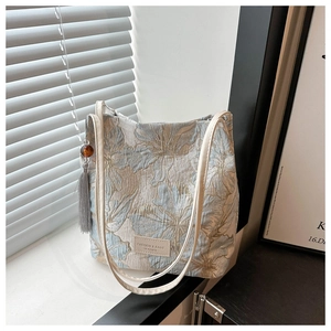 Détail du sac cabas brodé floral avec pompon et bandoulière en cuir près de la fenêtre