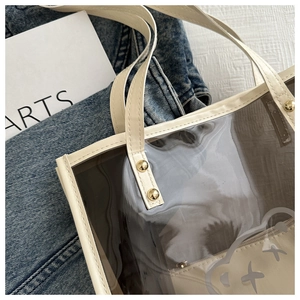 Détail du cabas transparent en PVC avec bordure crème et rivets dorés brillants
