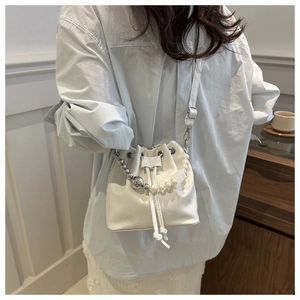 Detailed view of white bucket bag with decorative pearl and silver bead shoulder strap