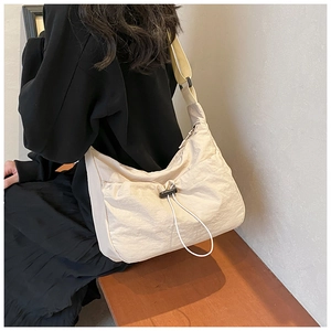 Detail view of a beige nylon crossbody bag with drawstring clasp and wide strap on a model