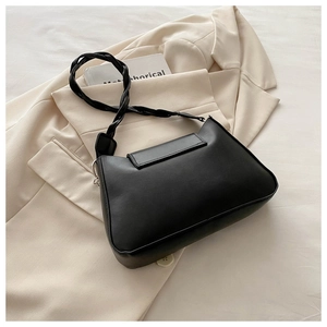 Detail of a black matte leather shoulder bag with a woven strap on a beige blazer