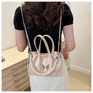 Detail of light pink satin bucket bag with pearl chain and silver butterfly charm decor