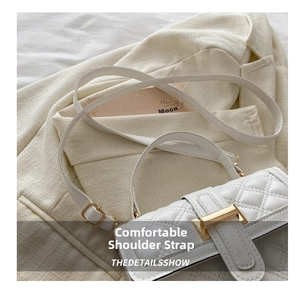 Detail of white quilted crossbody bag with golden clasp on beige blazer background
