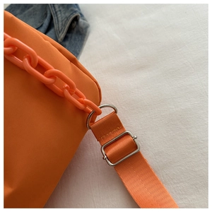 Detail of orange nylon bag featuring a thick decorative chain and adjustable woven strap