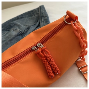 Detail of bright orange nylon crossbody bag featuring woven zipper pulls and plastic chain