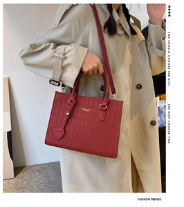 Detail of red faux leather tote bag with diamond pattern and heart-shaped pendant charm