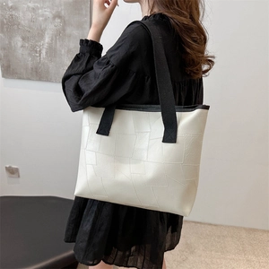 Minimalist beige quilted tote bag with black contrast strap worn by a model in interior