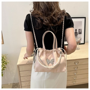 Detail view of pink satin bucket bag with pearl chain and silver butterfly charm decoration