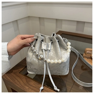 Detail of silver bucket bag featuring textured metallic finish and pearl bead handle