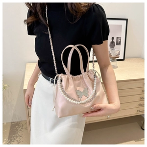Macro view of pink bucket bag featuring metallic butterfly and pearl chain details