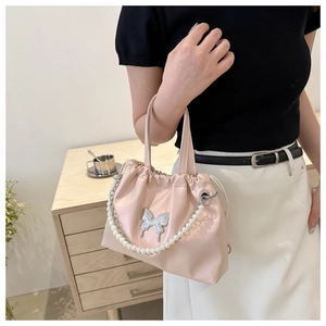 Detail of pink drawstring bucket bag featuring a silver butterfly charm and pearl chain