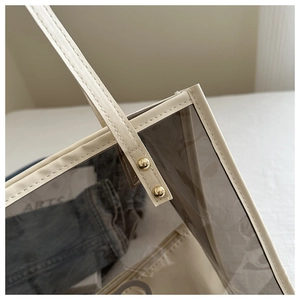 Détail d'un sac cabas transparent en PVC avec anses en cuir crème et rivets dorés polis