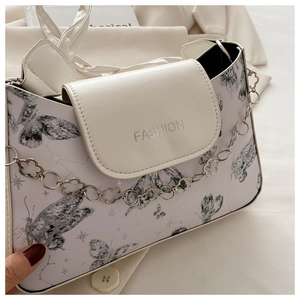 Close-up of white shoulder bag with black butterfly print and decorative flower chain