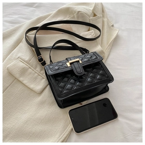 Detail of black quilted shoulder bag with gold metal buckle on beige blazer texture