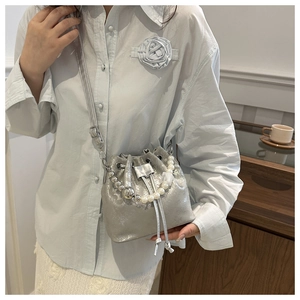 Détail du sac seau argenté avec poignée en perles et cordon porté par un mannequin