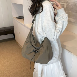 Olive green nylon crossbody bag with drawstring detail shown on a model in a minimalist room