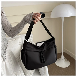 Detail view of a black tote bag featuring double woven drawstring and wide fabric shoulder strap