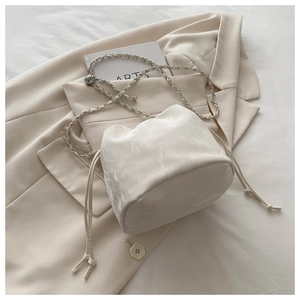 Detail view of cream drawstring bucket bag with wavy satin texture and chain strap