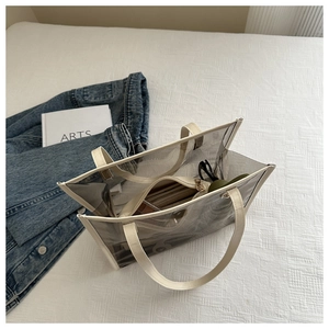 Détail du sac cabas en PVC transparent avec poignées en cuir et pochette sur le lit