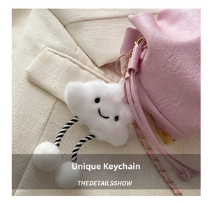 Close-up of a white fluffy cloud charm with smiling face and gold clip on a pink handbag