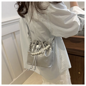 Silver metallic drawstring bucket bag with pearl strap worn as a stylish crossbody bag
