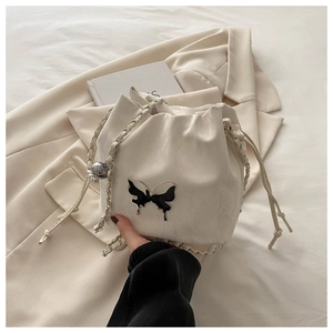 Detail of white pleated bucket bag featuring a metallic butterfly logo and chain strap