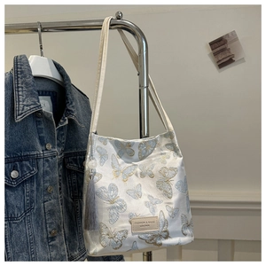 Broderie détaillée de papillons bleu et or sur sac seau en toile blanche avec gland