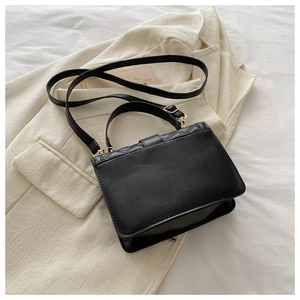 Detail of black quilted leather mini bag with metal buckle on a beige textured blazer