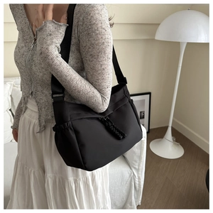 Detail of black nylon tote bag featuring decorative woven knots and adjustable wide strap