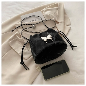 Detail of black marble bucket bag with silver butterfly accent on a beige blazer