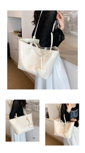 Detail of off-white textured leather tote bag featuring heart pendant and long shoulder straps