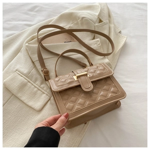 Detail of khaki quilted crossbody bag with gold buckle on a beige blazer background