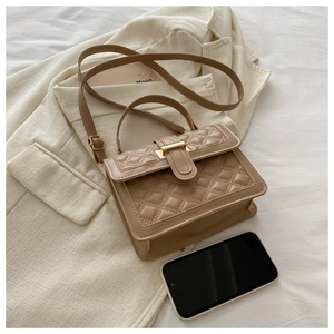 Close-up of quilted light brown shoulder bag with gold clasp on a beige blazer