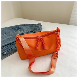 Detail of bright orange nylon cylinder bag with plastic chain and wide woven strap