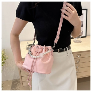Sac seau rose avec chaîne en perles porté par un mannequin dans un décor épuré
