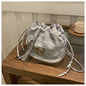Silver bucket bag with metallic butterfly detail and chain strap on a wooden table