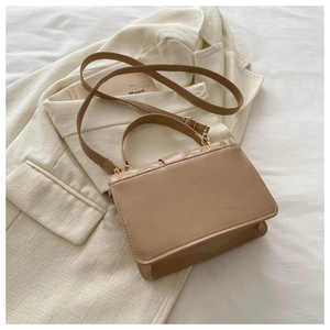 Detailed view of brown quilted crossbody bag with gold hardware on beige blazer background