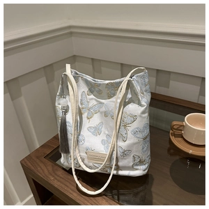 Détail de broderies papillons et pompon gris sur un sac cabas en toile blanche