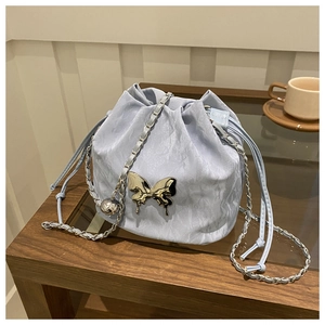 Light blue bucket bag with silver butterfly charm on a wooden table with coffee