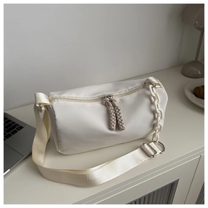 Close-up of cream Boston cylinder bag with textured fabric and unique brown woven zipper pulls