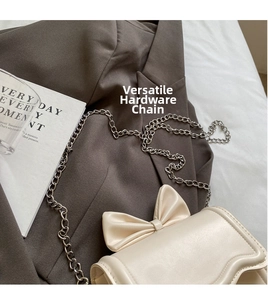Close-up of cream crossbody bag featuring a large bow and silver metal chain strap