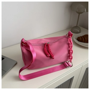 Detail of bright pink nylon crossbody bag showing wide strap and plastic chain decoration