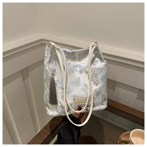 Détail du sac cabas en satin crème avec broderie papillon bleue et pompon gris