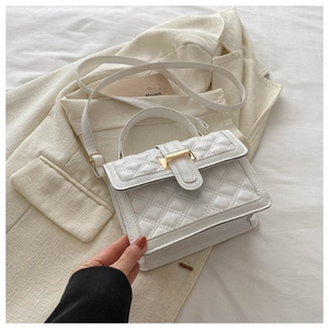Detail of white quilted crossbody bag with gold buckle on a cream blazer