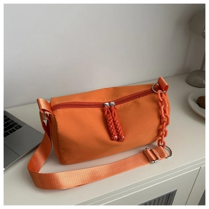 Detail of vibrant orange nylon crossbody bag with adjustable strap and chain link accessory