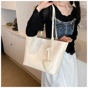 Detail of cream tote bag featuring textured leather finish and heart-shaped charm accessory