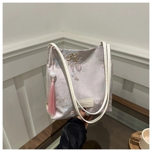 Détail de broderie sur sac en satin rose clair avec motifs floraux et pompons élégants