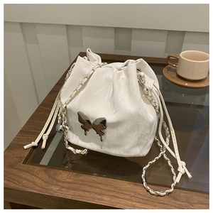 Detail of white drawstring bucket bag featuring wavy texture and silver butterfly ornament